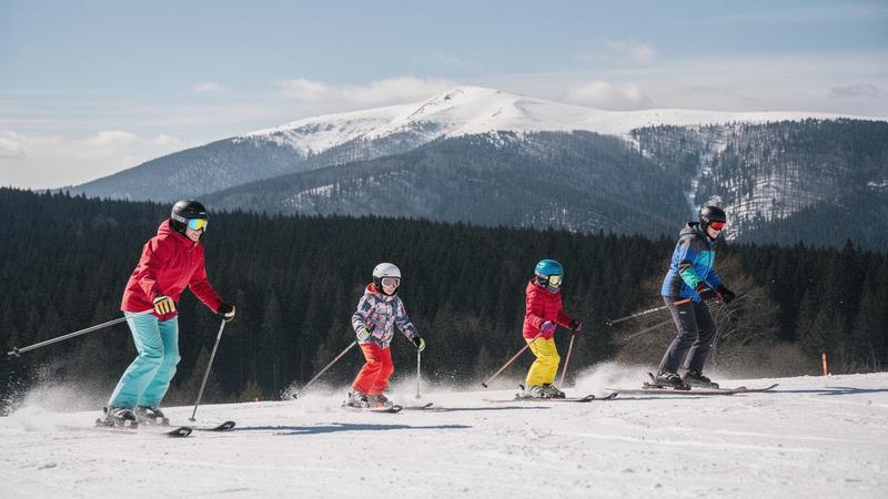 Family group skiing a groomed slope at a Carpathian resort